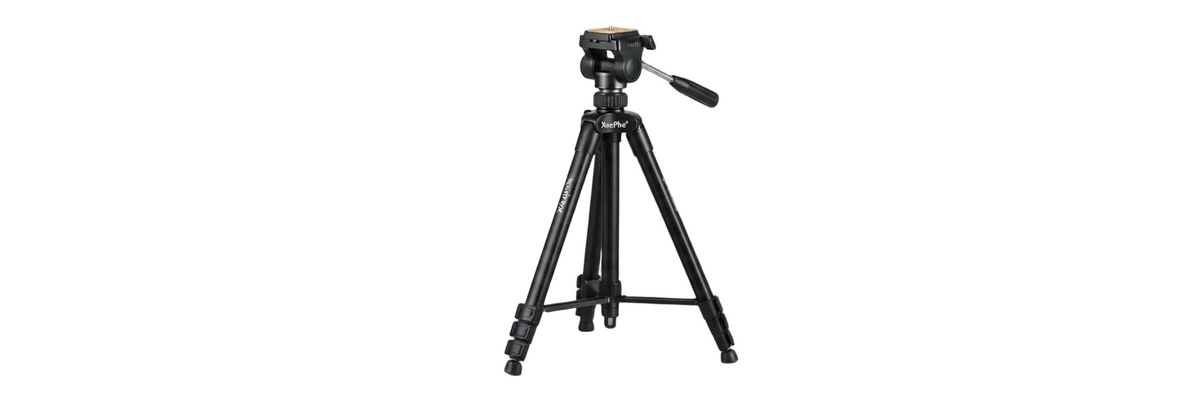 A black tripod with a mounted camera head and handle, standing on a gray surface against a misty white background.