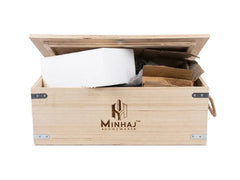 A light natural wood shoebox with a hinged lid, featuring the Minhaj Shoebox logo printed on the front, shown open with white and brown packing materials inside, set against a plain white background.